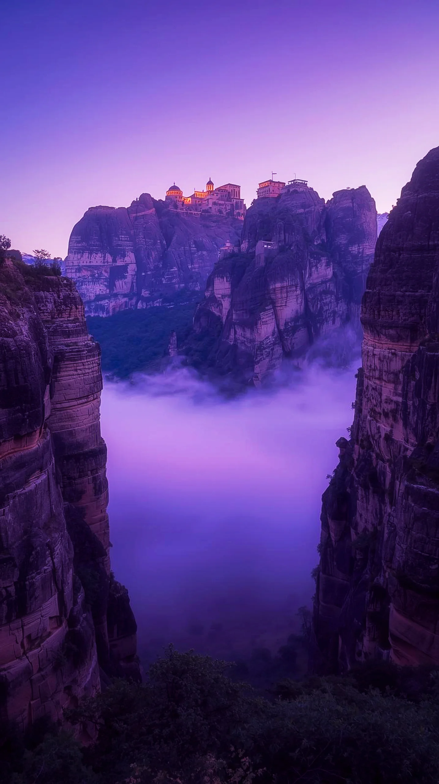 A breathtaking 4K mobile wallpaper of Meteora, Greece, featuring monasteries on cliffs above a sea of purple fog at