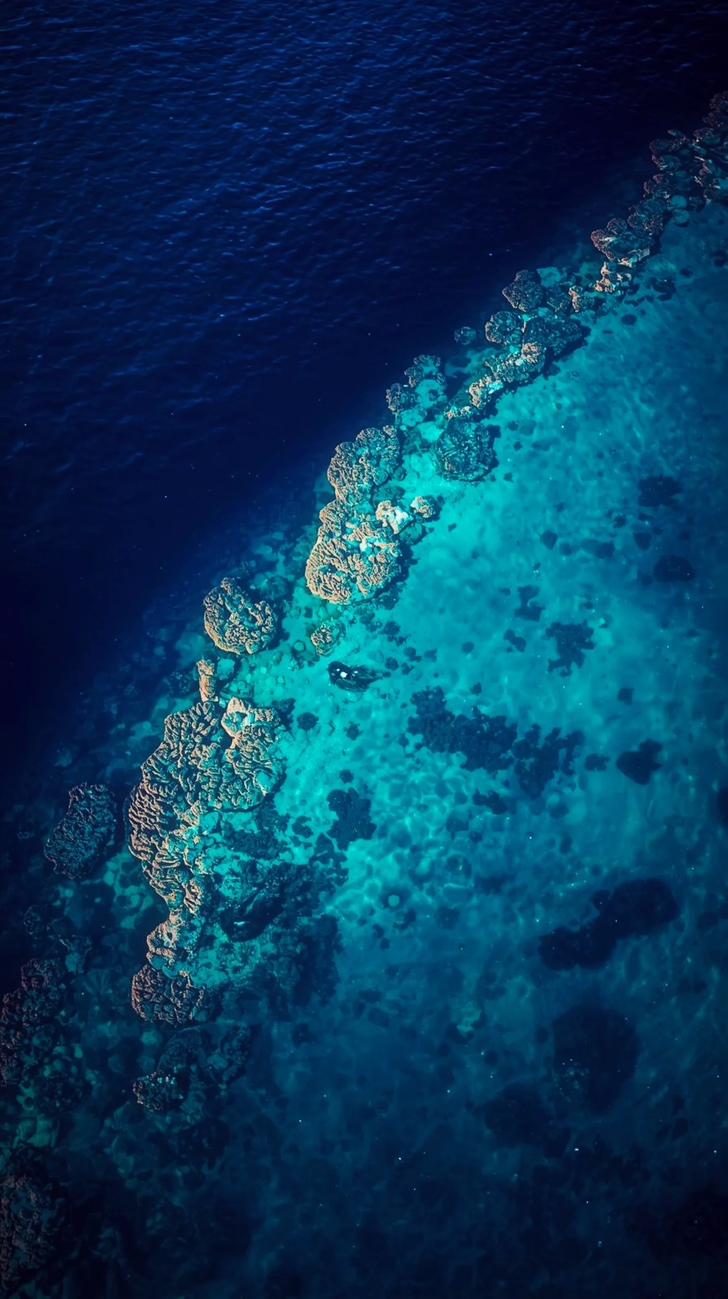 An aerial view of a coral reef in deep blue ocean water for mobile backgrounds.