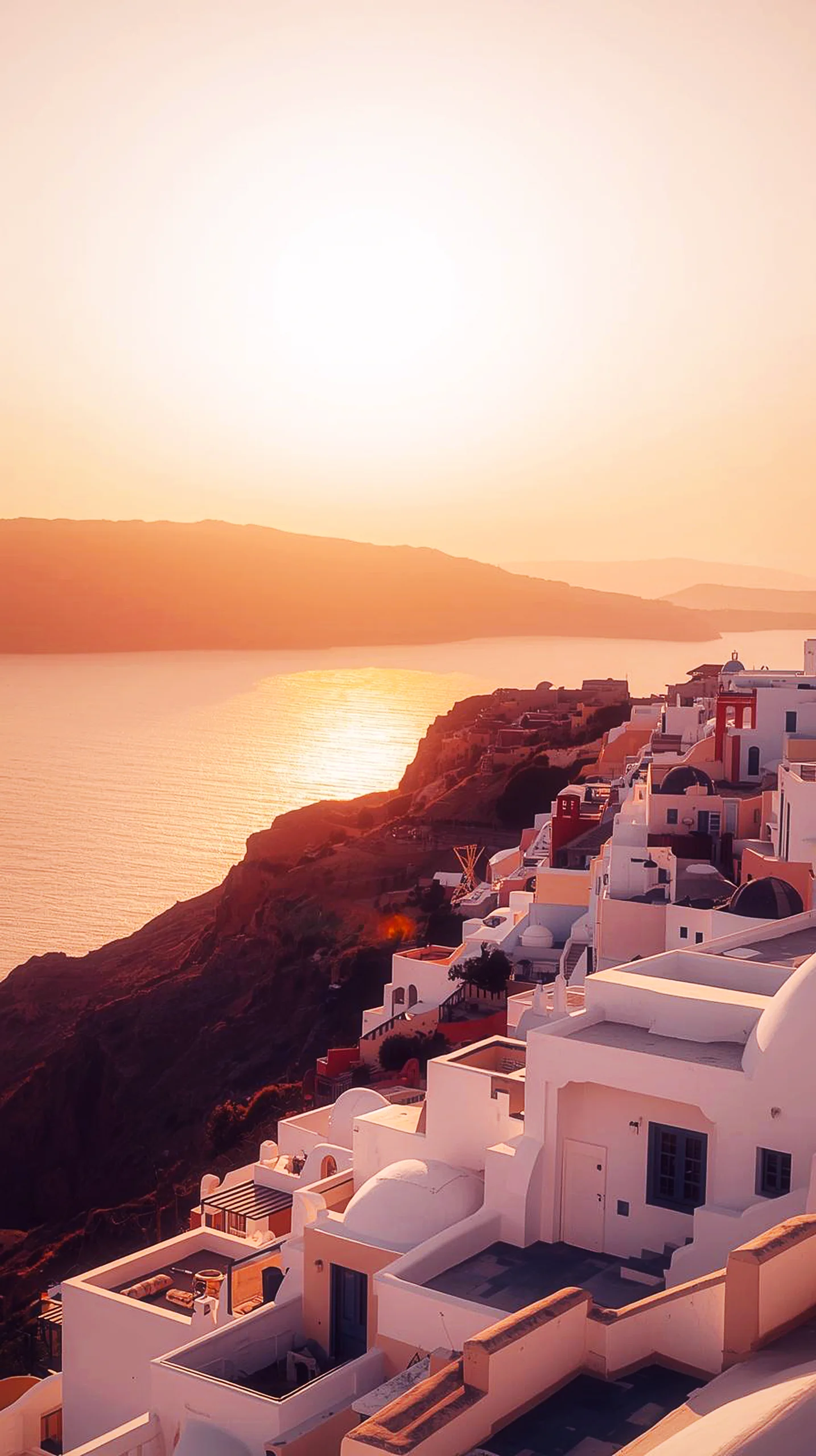 A stunning 4K mobile wallpaper of white Santorini buildings overlooking the ocean during a golden sunset.